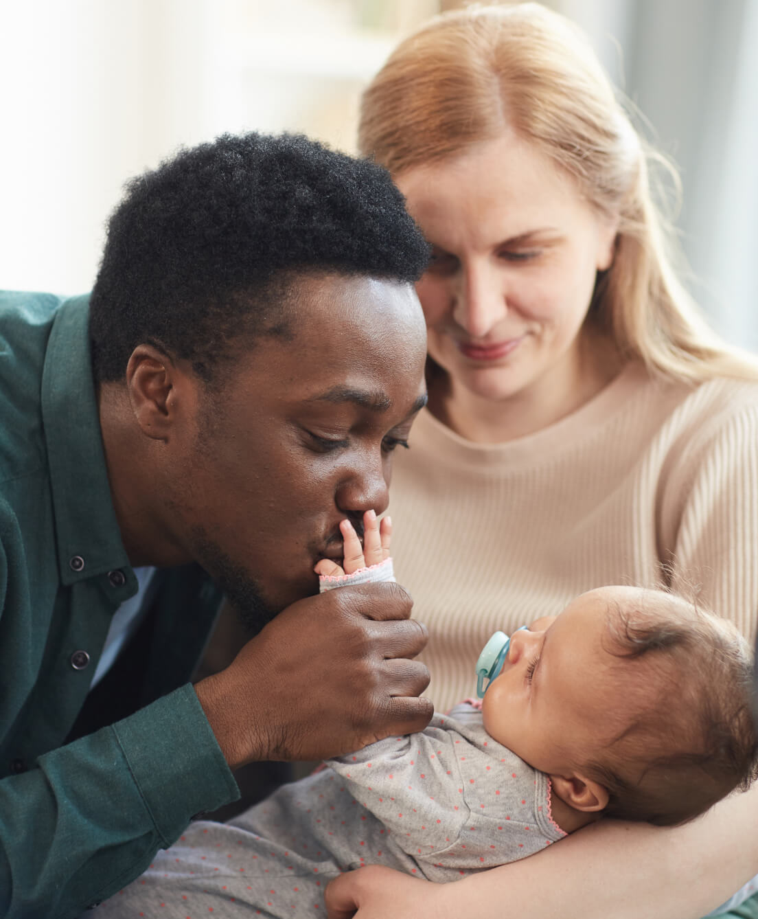 mom holding baby while dad kisses baby's hand