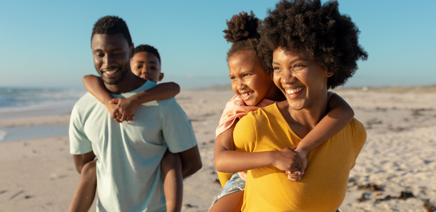 fmom and dad giving 2 kids piggyback rides on a beach