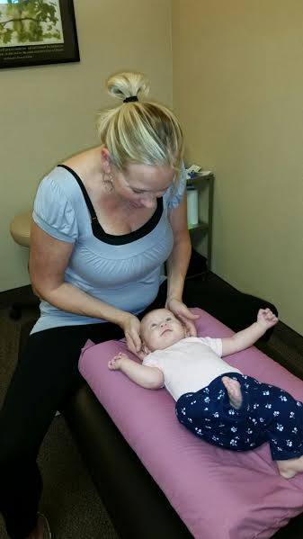 Dr. Lindsay Daniels sitting on a bench and working on the neck of a toddler laying in a pink bed at Go Health Chiropractic in Robbinsdale, MN