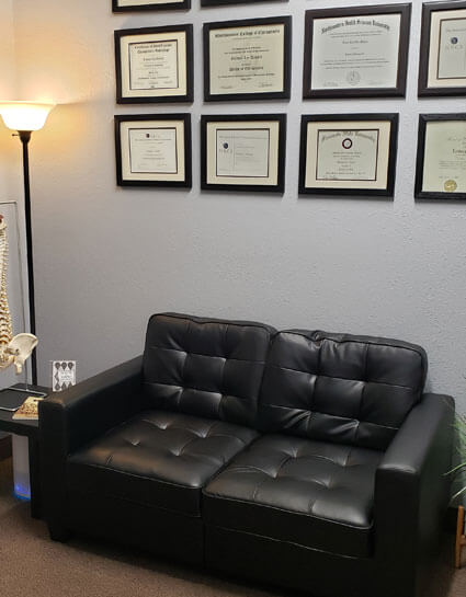 Black couch and brown carpet under a wall of diplomas and awards at Go Health Chiropractic in Robbinsdale, MN.