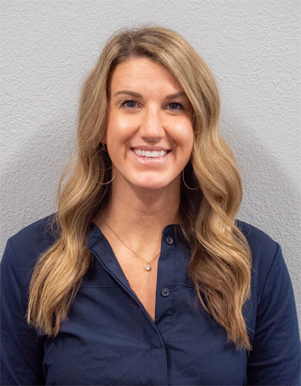 Dr. Nicole Des Marais wearing a navy blue button up in front of a white wall at Go Health Chiropractic in Robbinsdale, MN