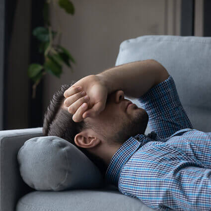 man-resting-on-couch-covering-face-with-arm-sq