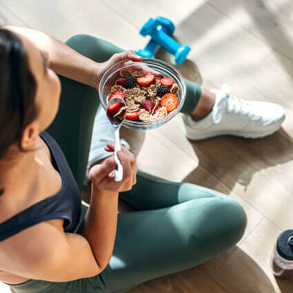 woman-in-workout-clothes-eating-bowl-of-oatmeal-and-berries-sq