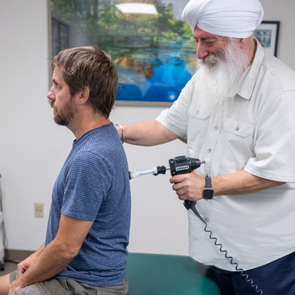 Dr. Khalsa adjusting a patient using a chiropractic tool