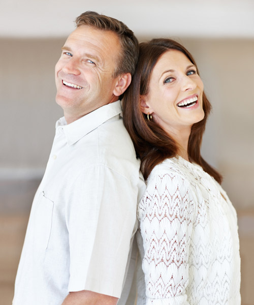 couple wearing white standing back to back smiling