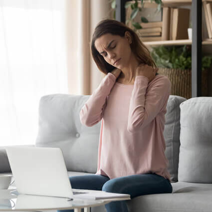 Person at a laptop holding the base of their skull, a common starting point for headaches that come from the neck