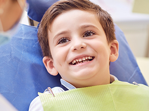 young boy smiling while sitting in dentists chair