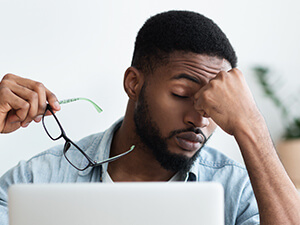 man sitting in front of laptop with headache pain