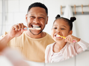 dad and daughter brushing teeth in mirror