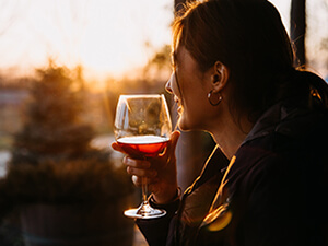 woman looking at a sunset with a glass of red wine
