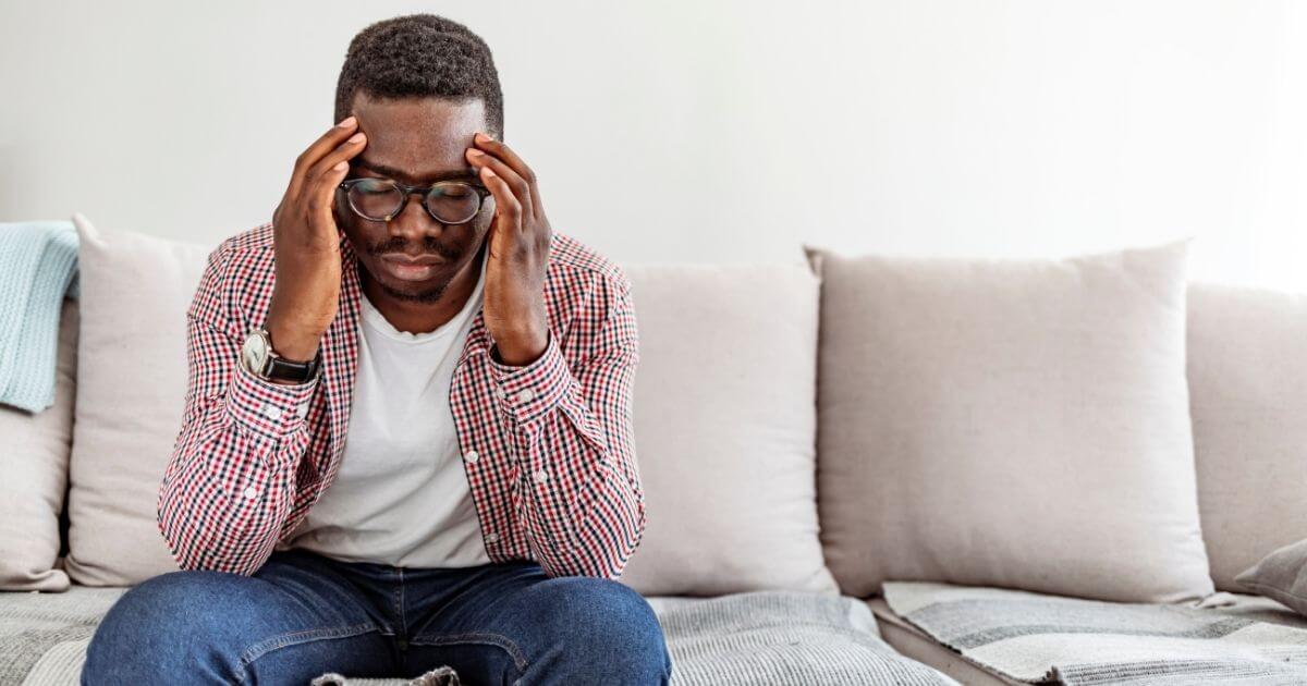 Man sitting with head pain on couch.