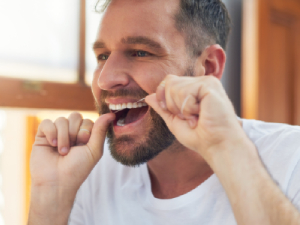 man flossing teeth in mirror