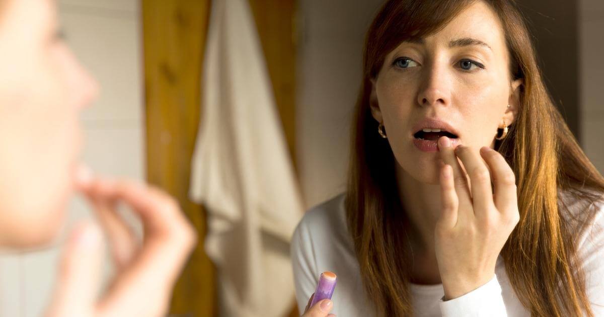 Woman applying lip balm in mirror.