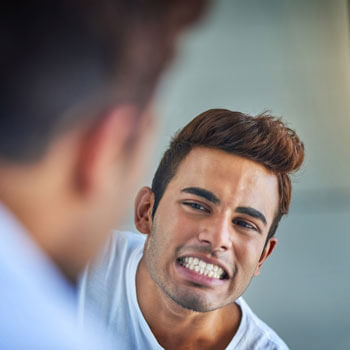 man looking at teeth in mirror