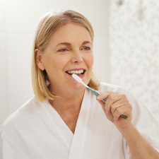 woman looking in mirror brushing teeth