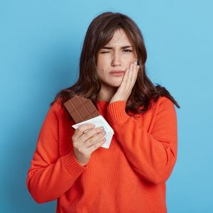 Woman eating candy bar in pain.