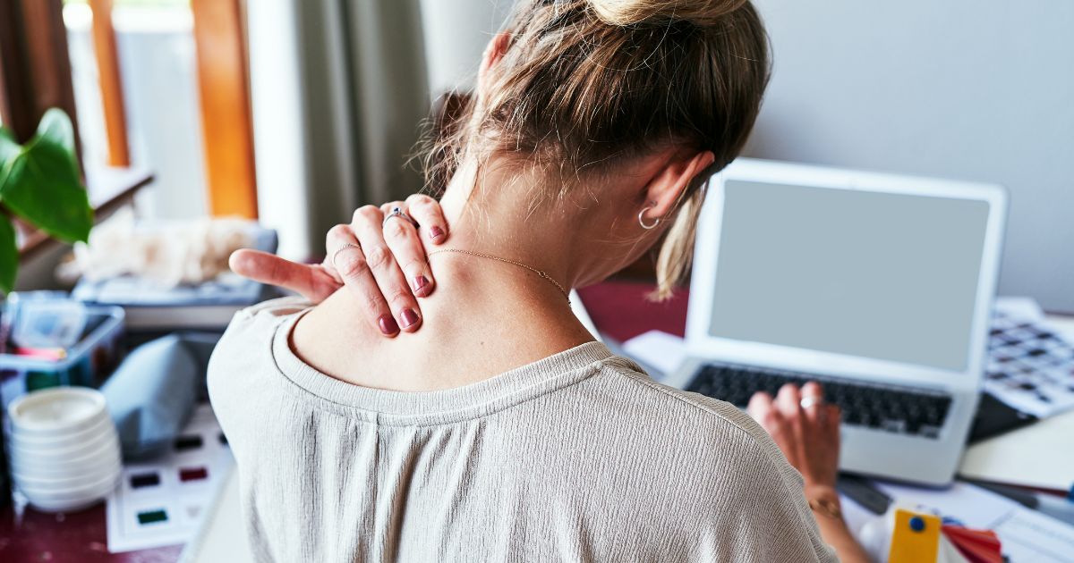 Woman sitting at desk grabbing neck.