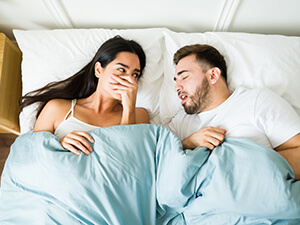 woman reacting to man having bad breath while in their bed