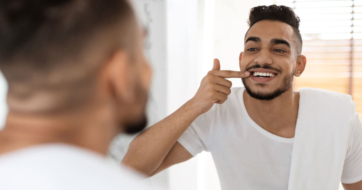 man checking teeth in mirror