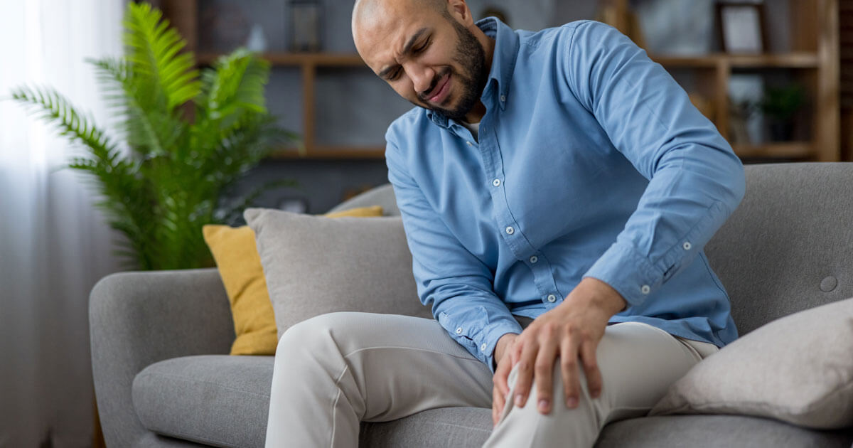 man on couch holding knee in pain