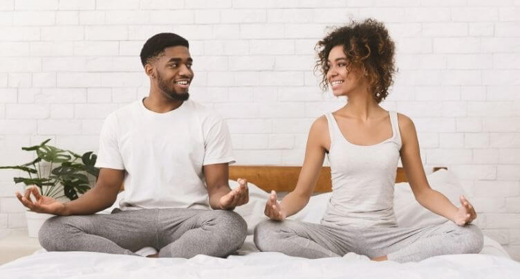 Man and woman meditating in bed.