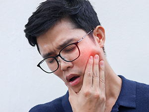 man wearing glasses with jaw pain rubbing chin