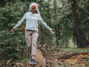 woman walking in woods balancing on a log