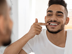man looking at teeth in mirror