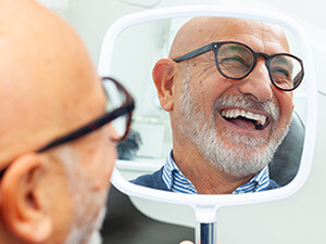 man with glasses smiling in a hand mirror