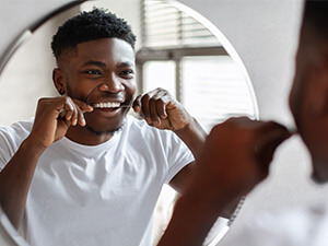 man flossing teeth in a bathroom mirror