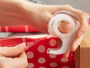 person using tape cutter to wrap a gift