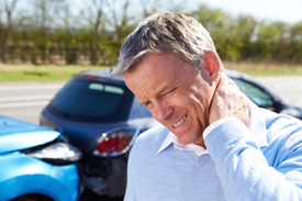 Photo of a man holding his neck with an auto accident in the background
