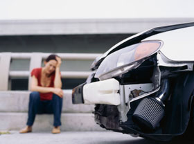 woman sitting next to a car with a damaged bumper