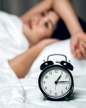 Alarm clock in focus with a restless sleeper in the background