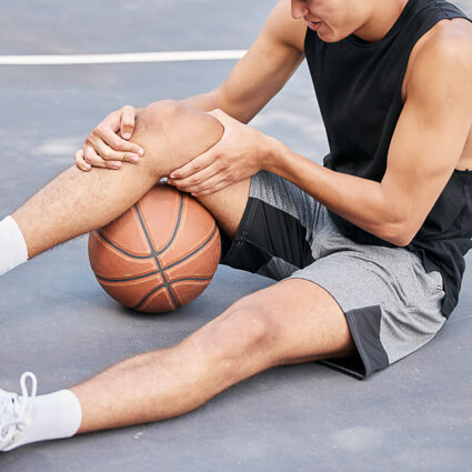 man playing basketball sitting on the floor holding knee in pain