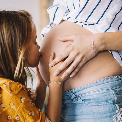big sister kissing pregnant belly of mother