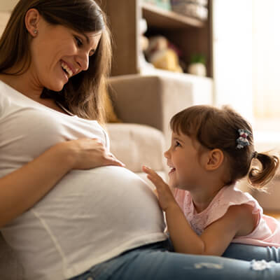 Pregnant woman and daughter laughing and touching her belly