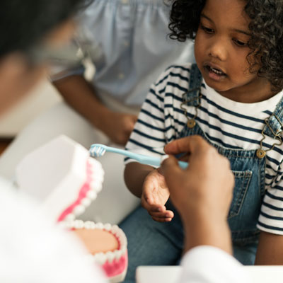 Dentist showing little girl how to brush her teeth