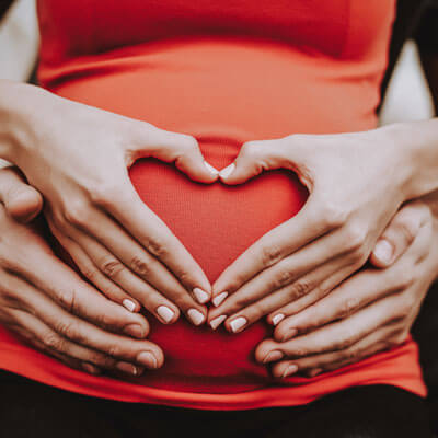 closeup of hands of hands making a heart on pregnant belly