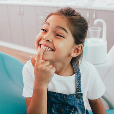 little girl smiling at dental office pointing at her teeth