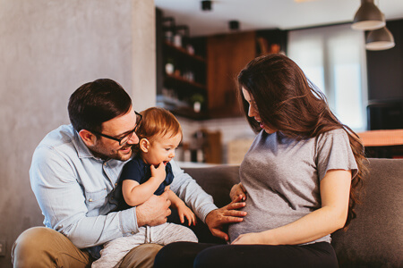 Pregnant woman on the couch with her husband and young child