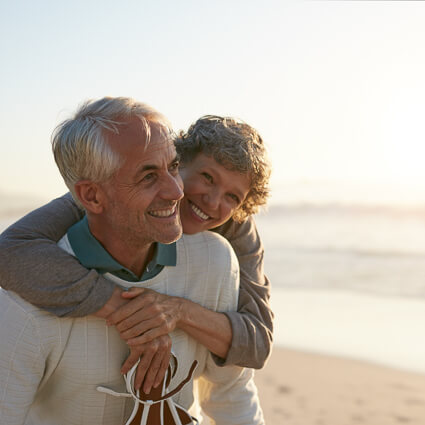 older man and woman hugging while walking on a beach