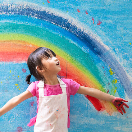 smiling kid with rainbow art behind her