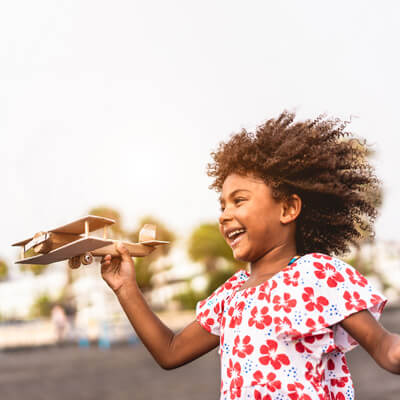 Girl pretending to fly a small wooden airplane model
