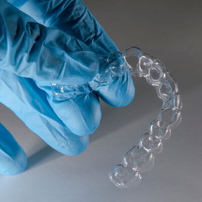 gloved hand holding clear aligner