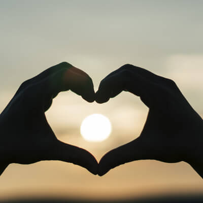 hands making a heart shape around the sunset in the background