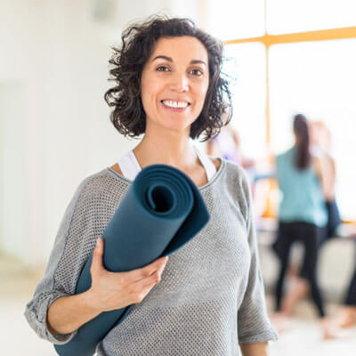Woman holding yoga mat and smiling.