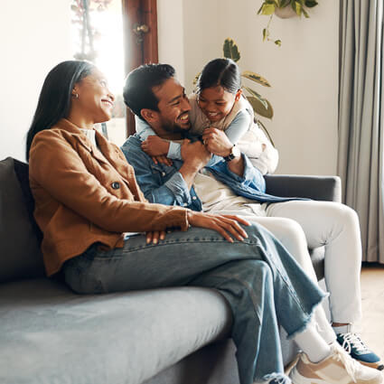family of 3 smiling and sitting on sofa together