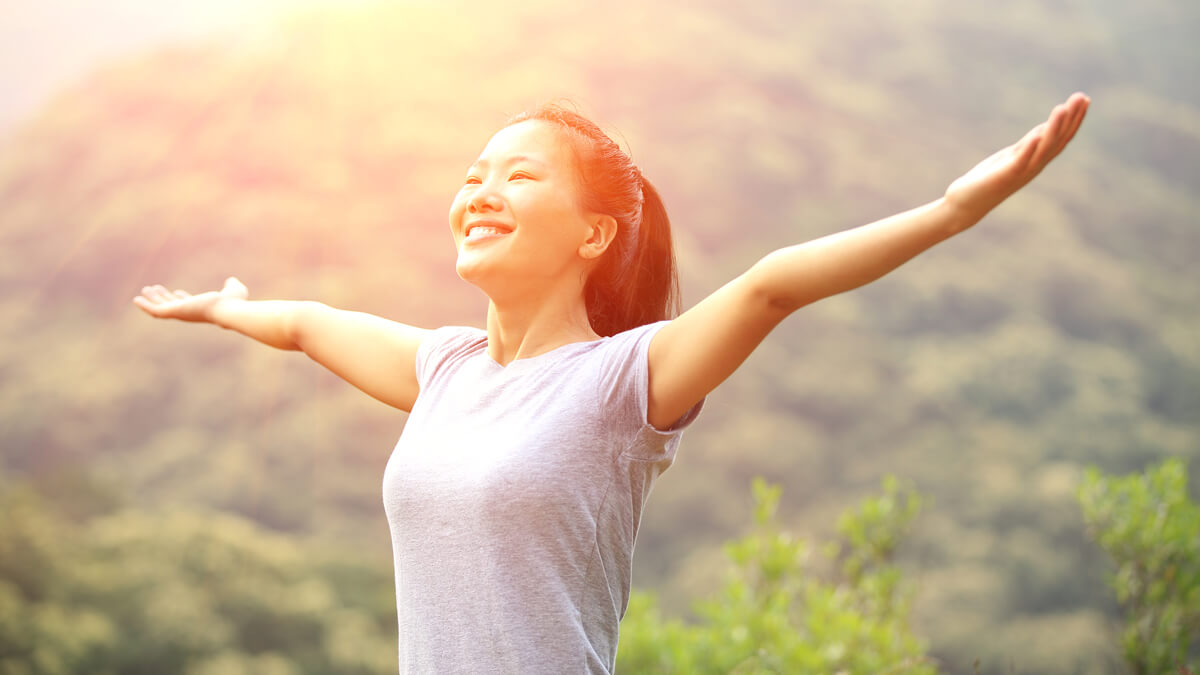 Woman on a mountain raising her hands to the sun