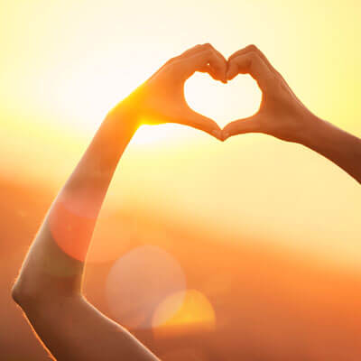 Hands help to the sun in a heart shaped during sunset